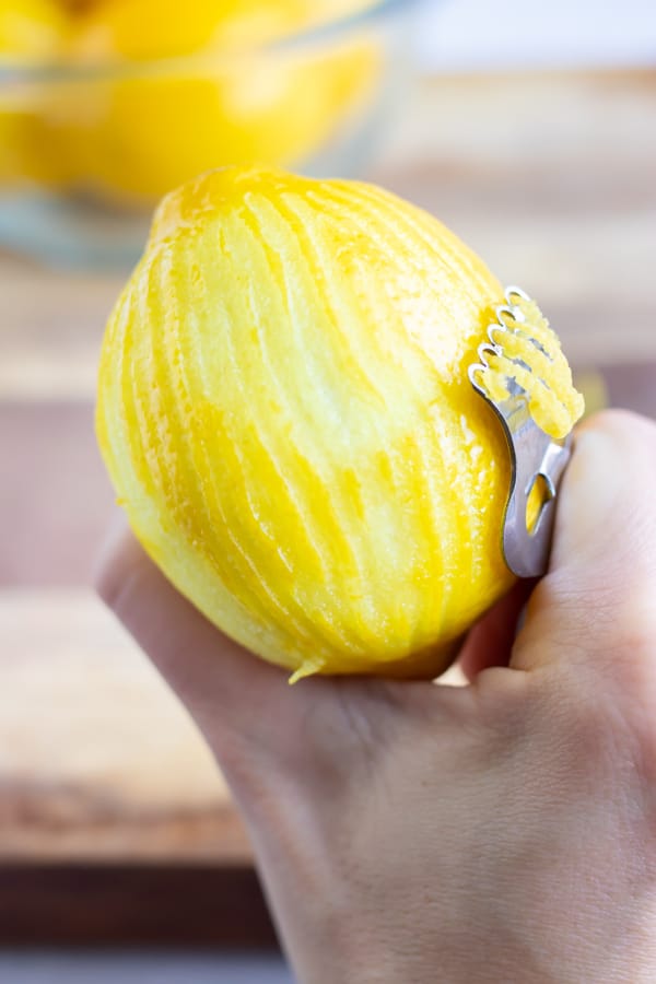 A hand zesting a lemon using a citrus zester.