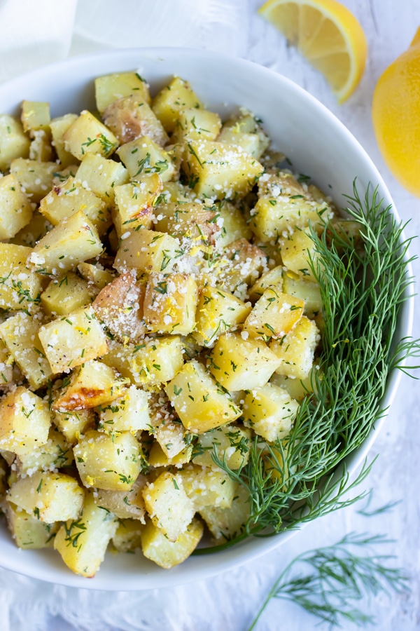 A large white bowl full of roasted potatoes with a lemon dill butter sauce and Parmesan cheese.
