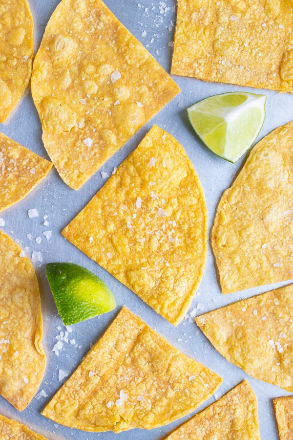 A baking sheet with homemade tortilla chips in a single layer with salt and limes.
