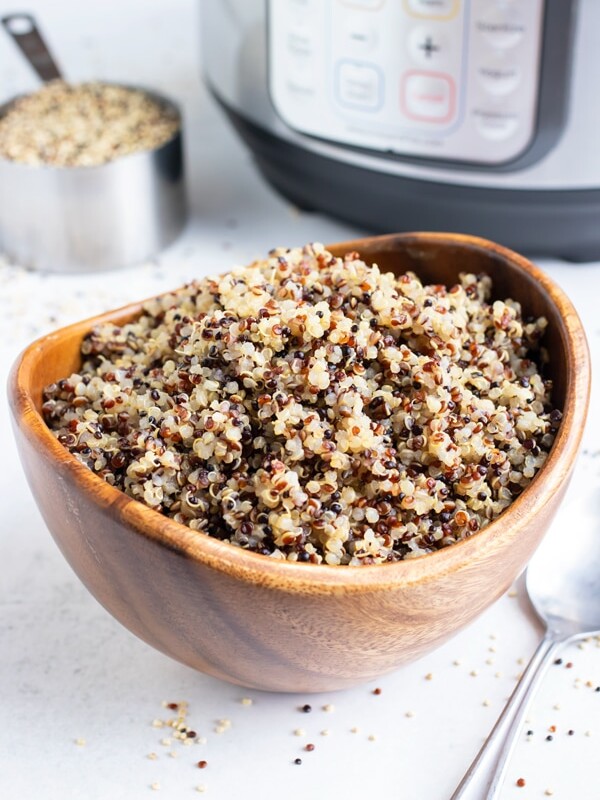 A wooden bowl full of cooked tri-color quinoa with an Instant Pot.