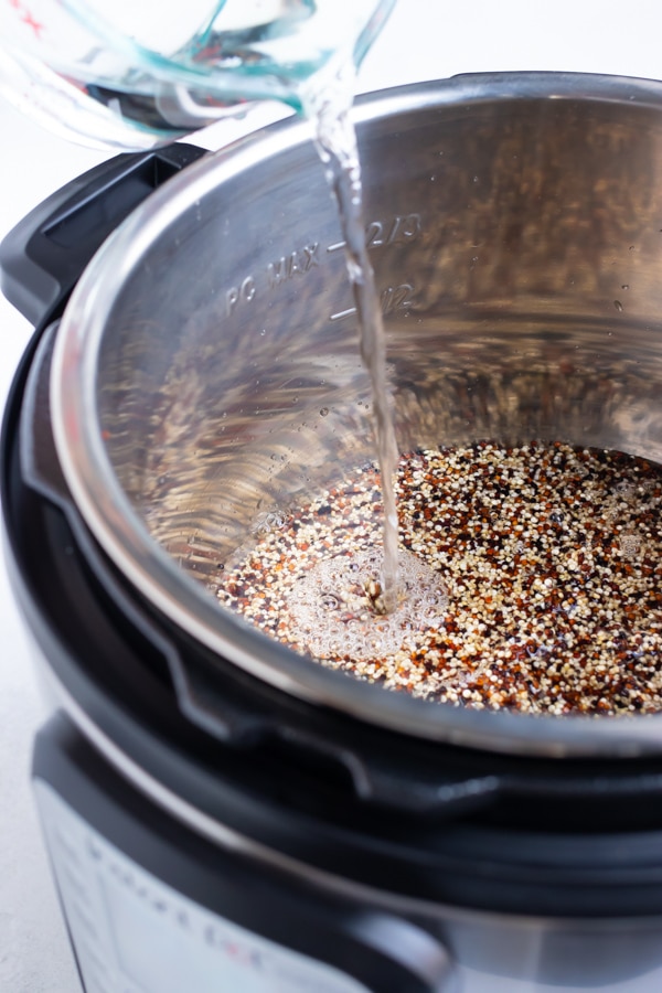 Water being poured into an Instant Pot full of quinoa.