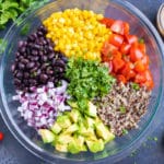 A glass bowl full of black beans, corn, tomatoes, quinoa, avocado, and red onions.