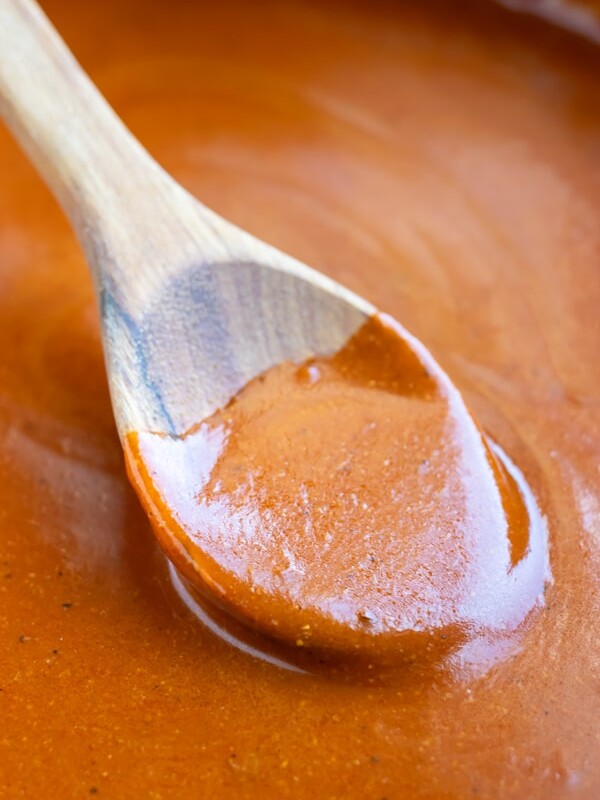 A wooden spoon stirring a red enchilada sauce.