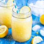 Homemade frozen lemonade in a glass mason jar with a blue straw next to a lemon wedge.
