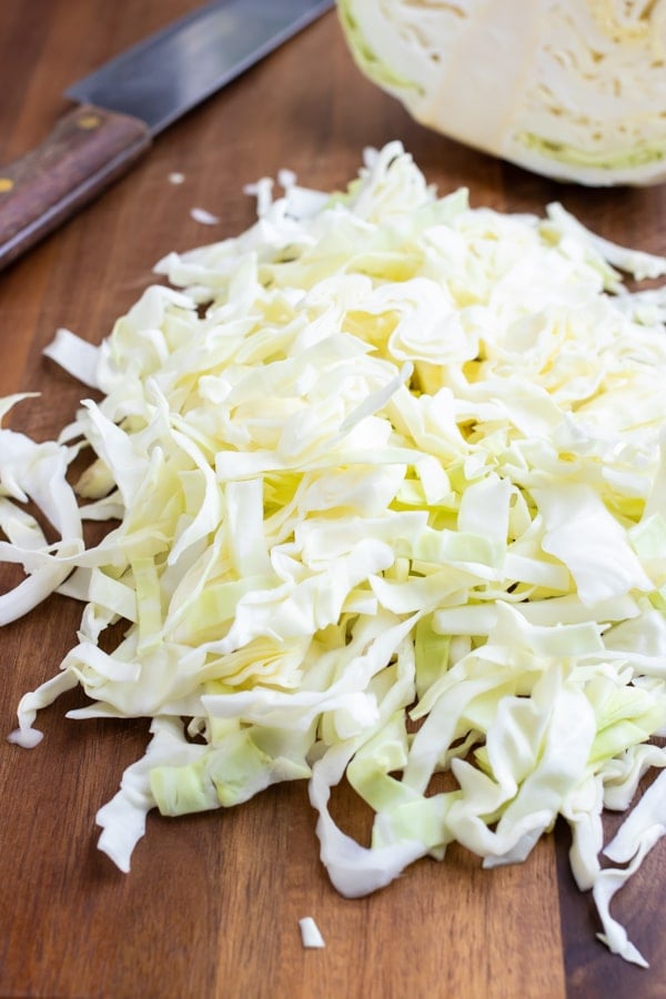 A pile of cut and shredded cabbage on a cutting board to be used in a coleslaw recipe.