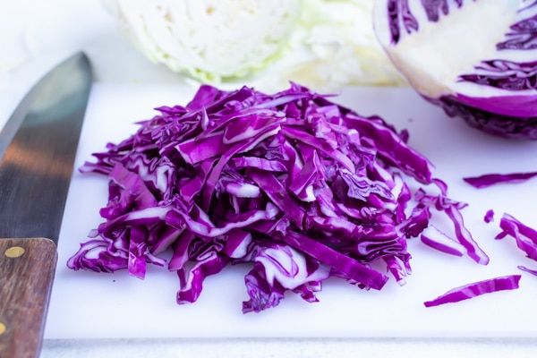 Thinly sliced red cabbage on a white cutting board with a wedge in the background.