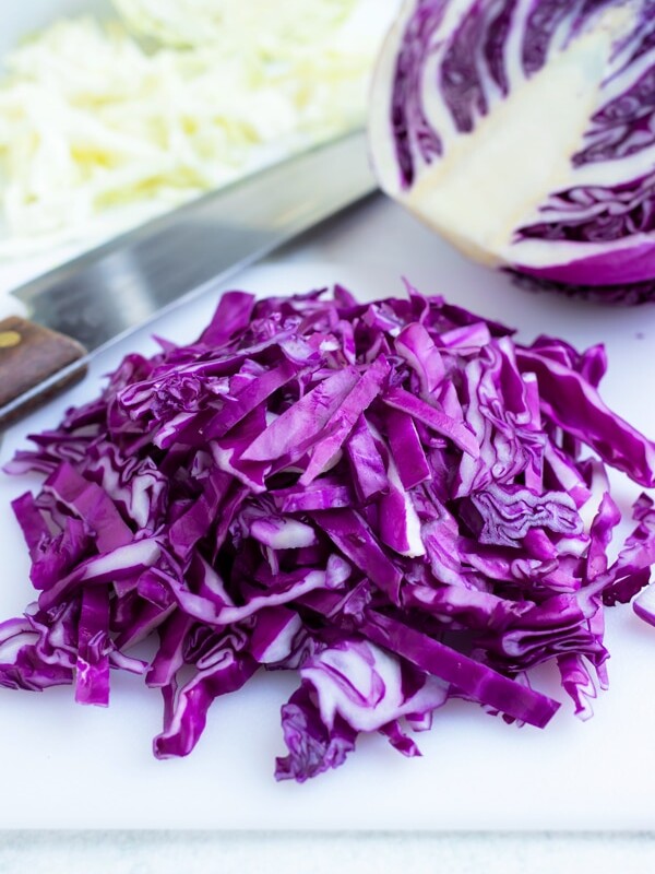 Thinly sliced red cabbage on a white cutting board with a wedge and a knife in the background.