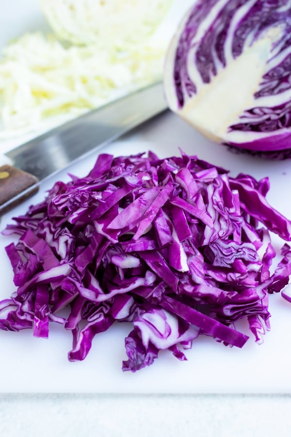 Thinly sliced red cabbage on a white cutting board with a wedge and a knife in the background.