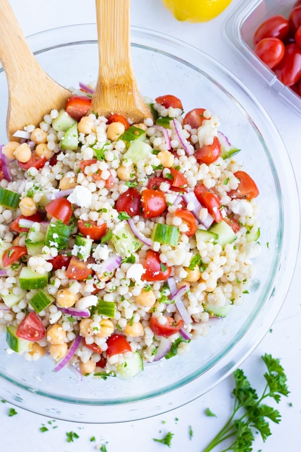 A big glass bowl full of a Mediterranean Couscous Salad with tomatoes, feta, garbanzo beans, and cucumbers.