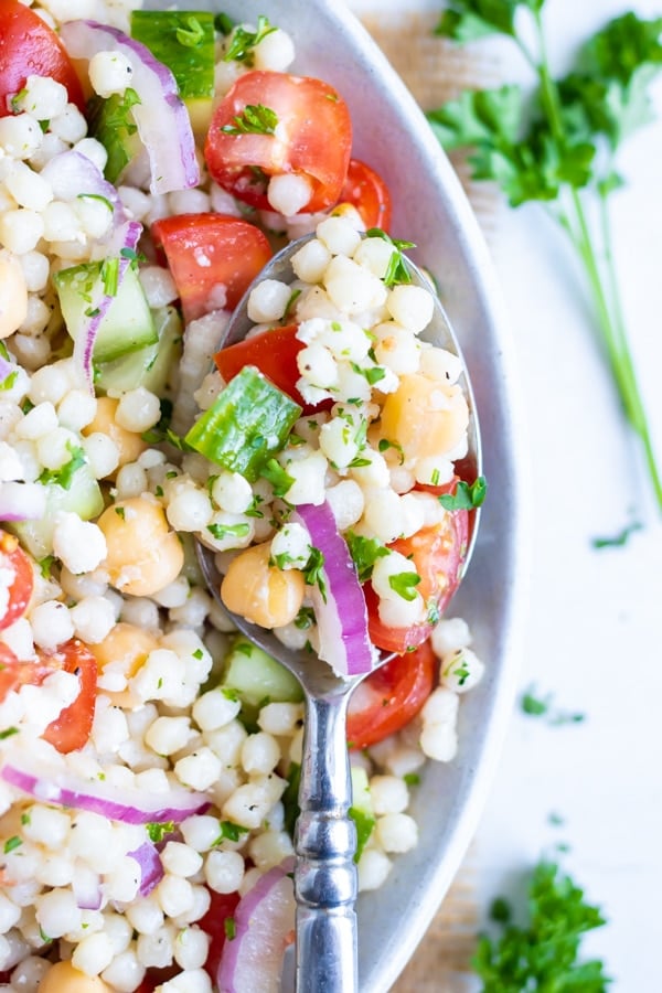 A spoon scooping out a bite of a cold Mediterranean couscous salad from a bowl.