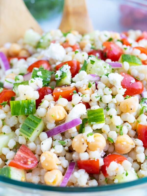 A big glass bowl full of a Mediterranean Couscous Salad with tomatoes, feta, garbanzo beans, and cucumbers.