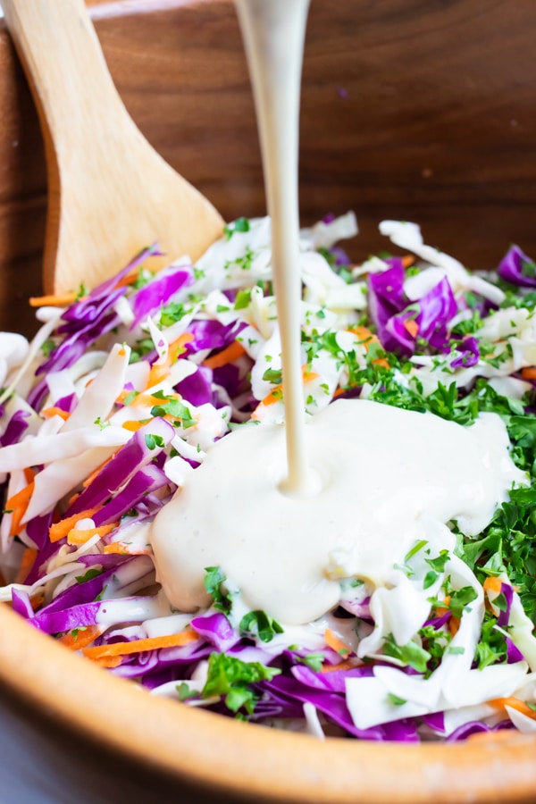 Coleslaw dressing with mayonnaise and mustard being poured over shredded cabbage.