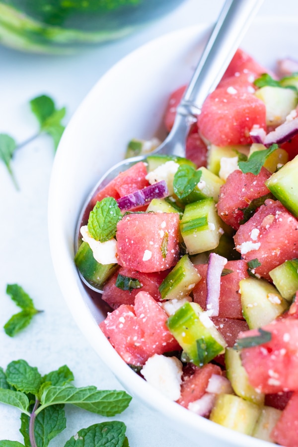 A spoon in a white bowl scooping out a serving of a watermelon fruit salad for a July 4th picnic.