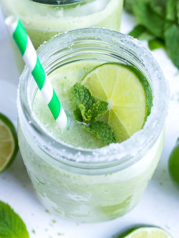A sugar-rimmed glass with a frozen mint cocktail with a lime slice on top and a paper straw.