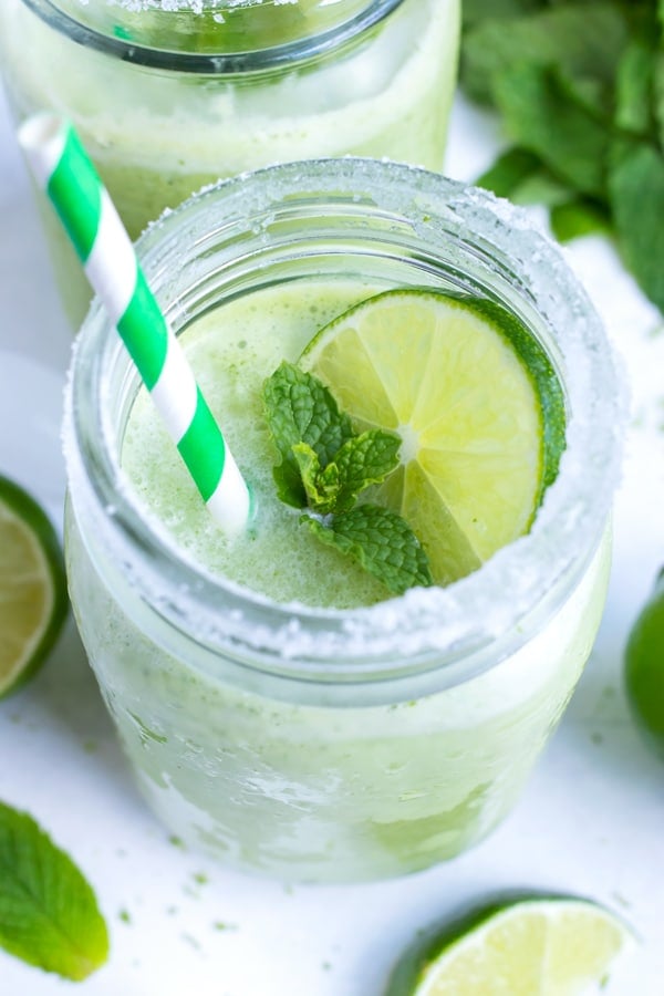 A sugar-rimmed glass with a frozen mint cocktail with a lime slice on top and a paper straw.