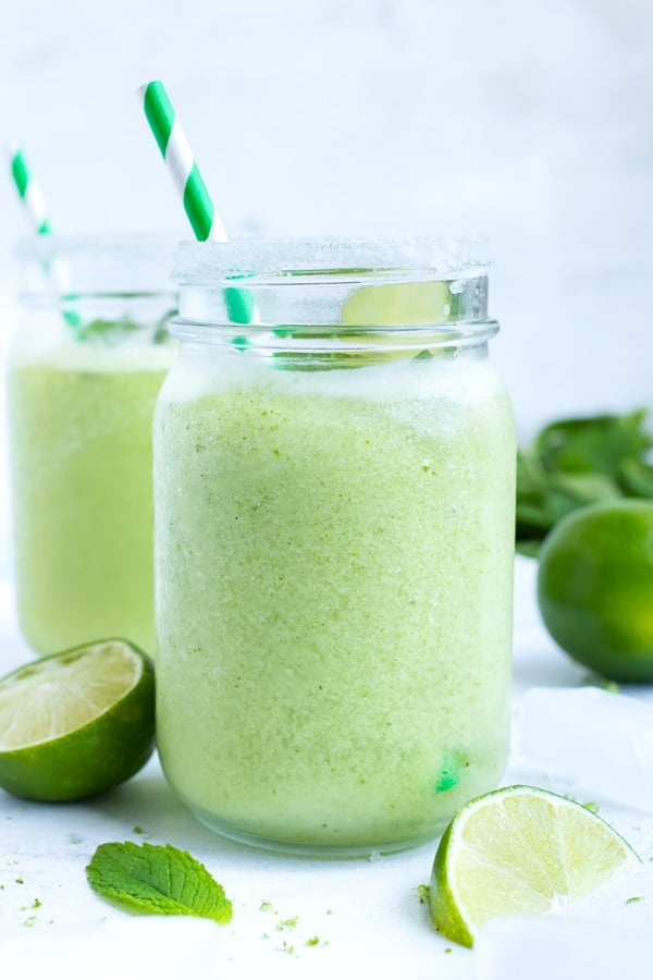 Two mason jar glasses full of a frozen mojito with fresh mint.