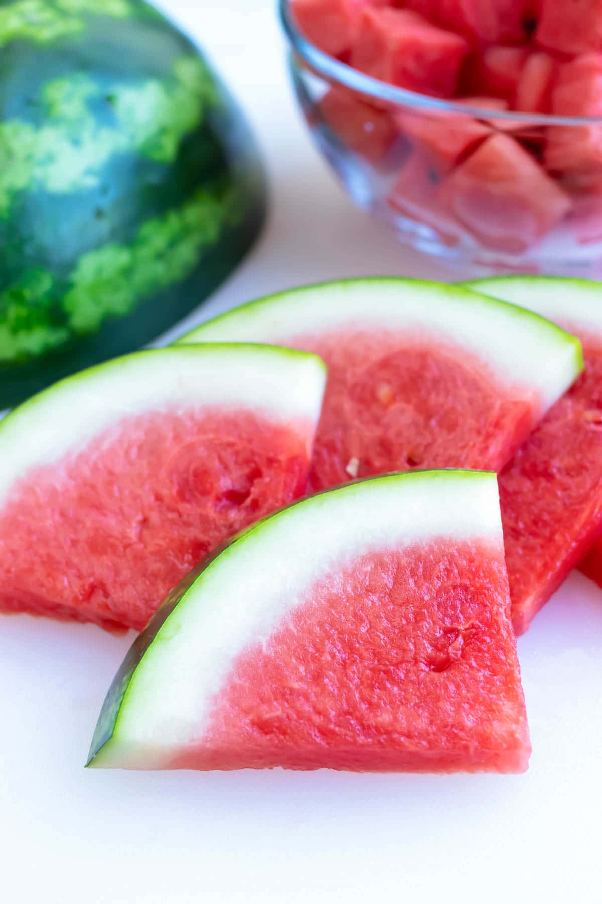 A pile of watermelon slices with a full melon in the background.