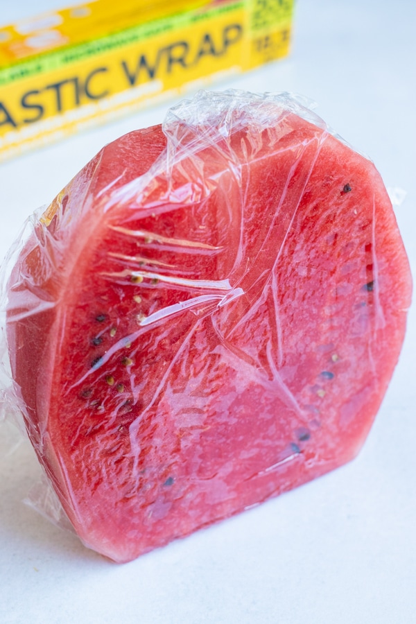 Half of a watermelon wrapped in plastic wrap to be stored in the refrigerator.