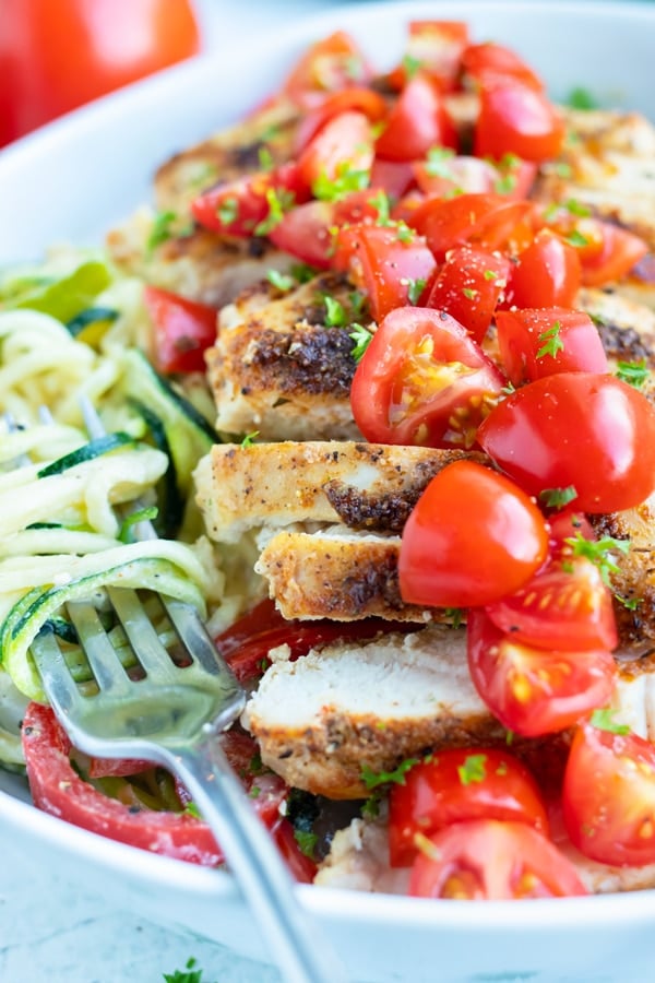 Sliced cajun chicken, tender vegetable noodles, topped with chopped tomatoes are in a bowl for an easy main dish.