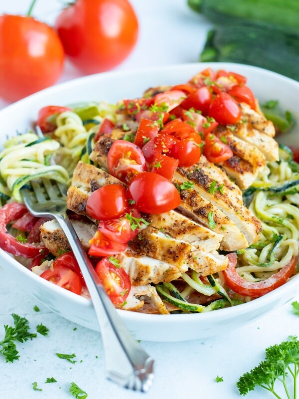 Cajun chicken zoodles in a bowl are topped with fresh tomatoes and parsley for a low-carb and Whole30 meal.