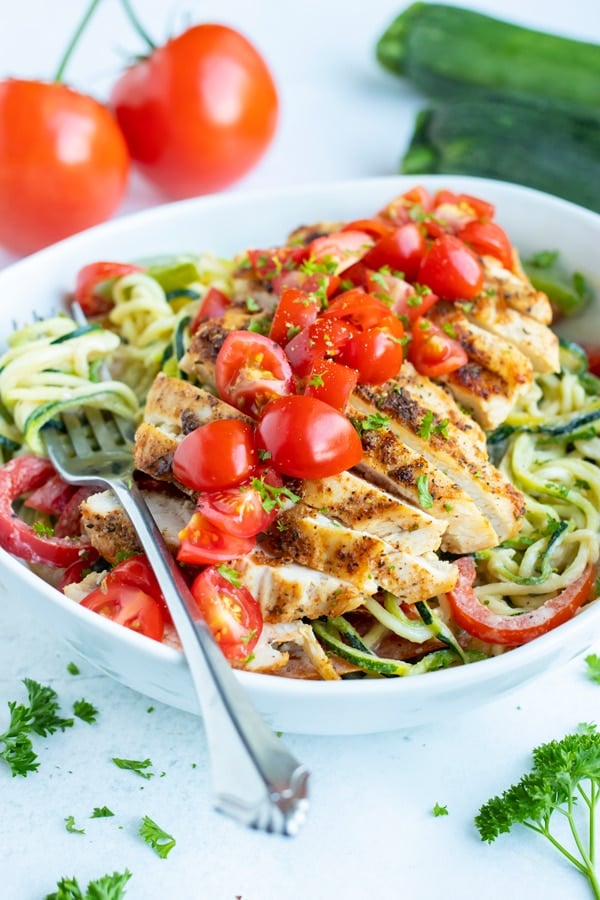 Cajun chicken zoodles in a bowl are topped with fresh tomatoes and parsley for a low-carb and Whole30 meal.