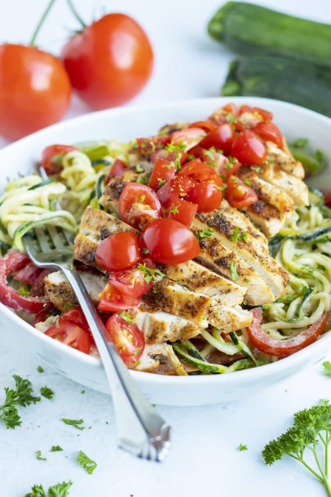 Cajun chicken zoodles in a bowl are topped with fresh tomatoes and parsley for a low-carb and Whole30 meal.