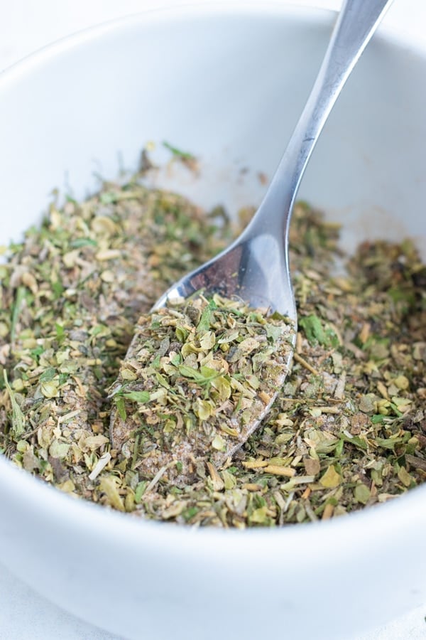 Greek seasoning mix is being scooped out of a small bowl with a spoon.