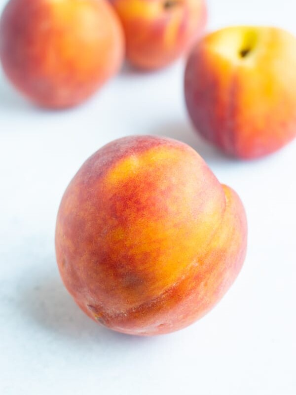 A couple whole peaches are resting on a white counter.