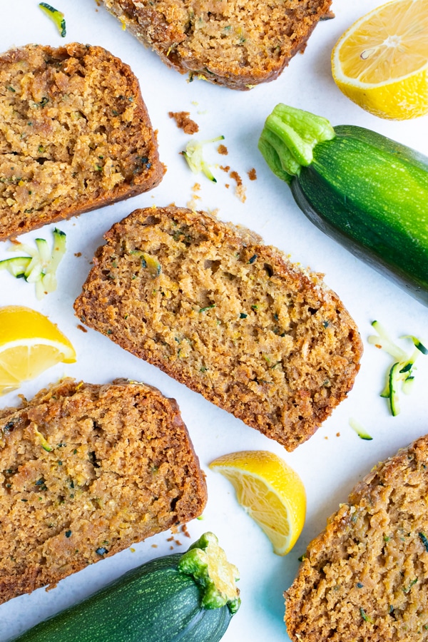 Moist slices of healthy zucchini bread laying flat on the counter next to lemons and zucchini.