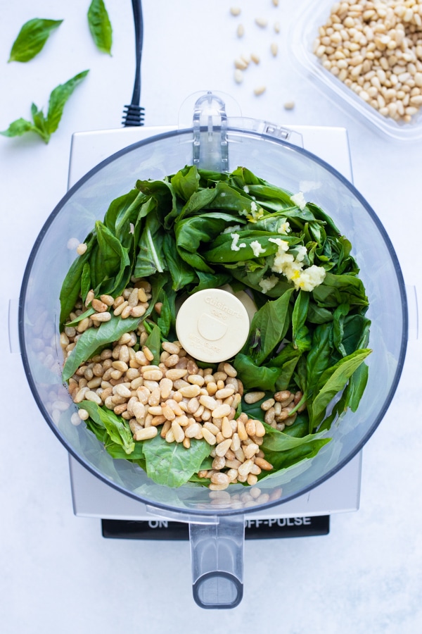 Pine nuts, fresh basil leaves, parmesan cheese, and other ingredients are placed in a food processor to create a smooth pesto sauce.