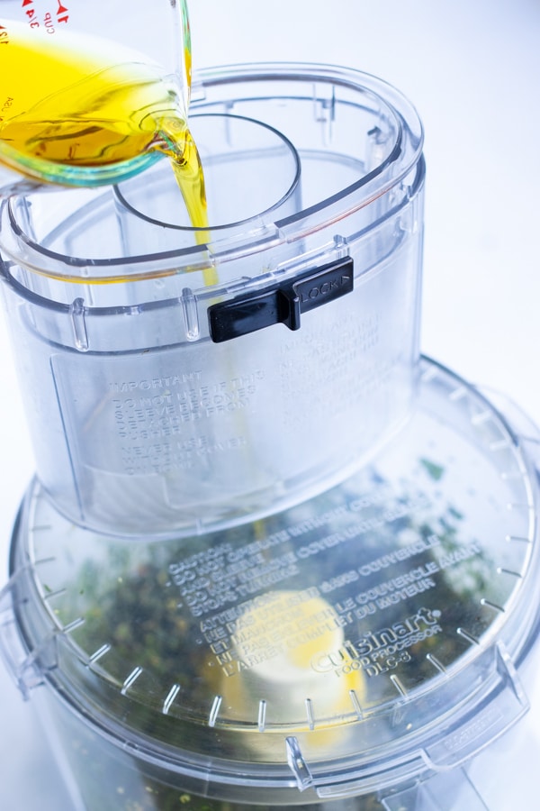 Olive oil is poured into the food processor while blending all other ingredients.