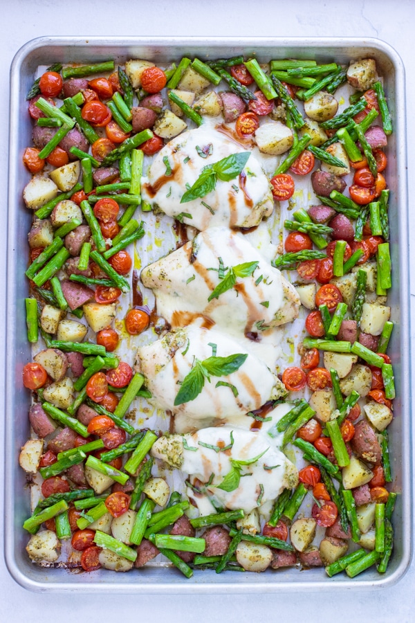 Once all ingredients in this sheet pan caprese meal have been cooked the chicken is drizzled with a balsamic vinegar glaze and topped with fresh basil.