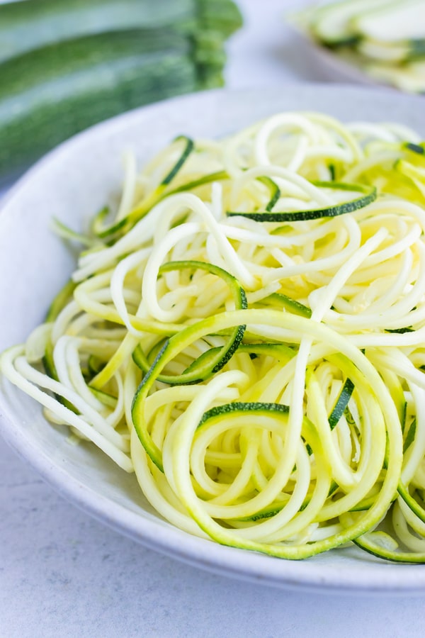 A big pile of spiralized zucchini in a bowl in preparation for recipe using zucchini noodles.