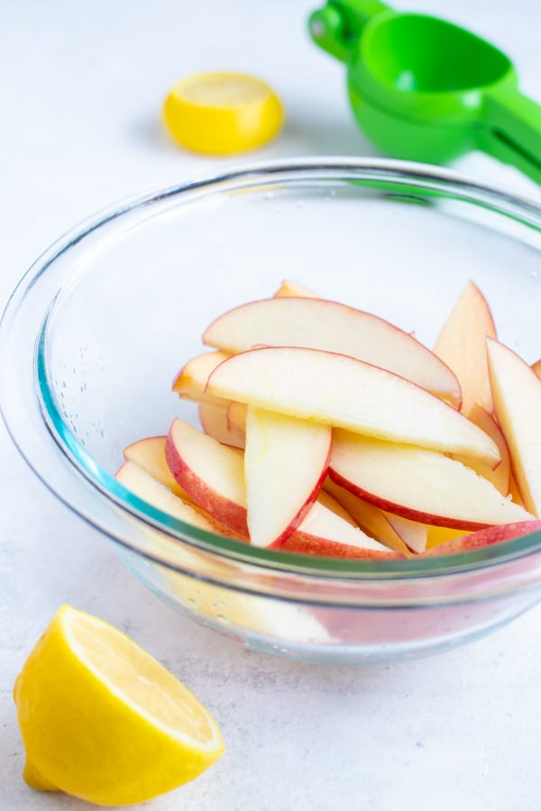 Fresh apple slices are placed in a bowl and tossed in lemon juice to prevent browning.