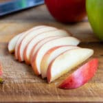 Apple slices are laid out in a row on a cutting board before being used in favorite recipes.