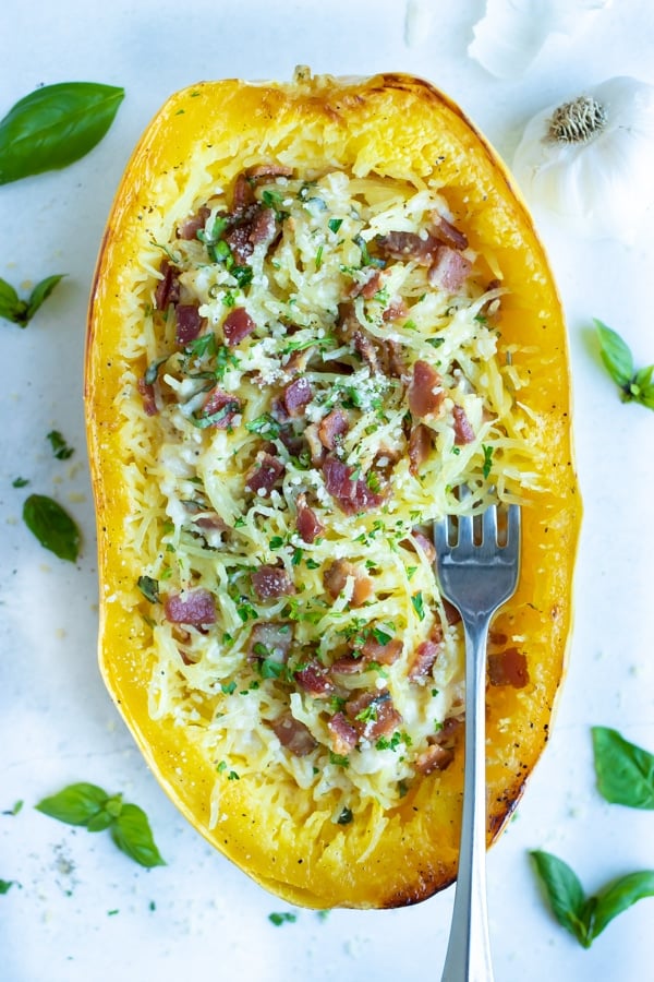 Spaghetti squash is topped with carbonara sauce, bacon, and fresh basil for a healthy dinner.