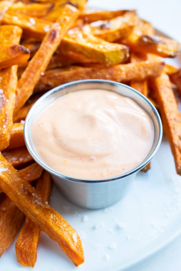 A container of homemade Sriracha Mayo on a plate with sweet potato fries.