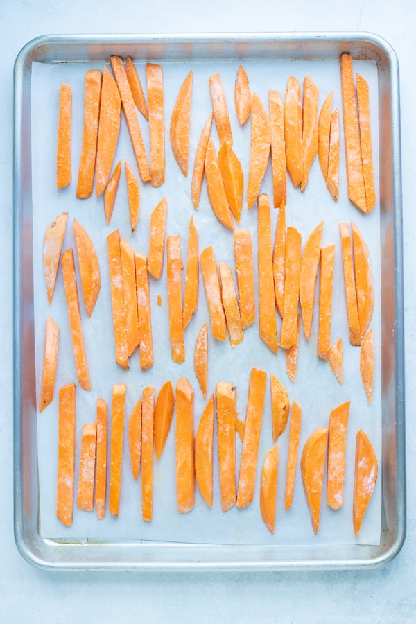 Sweet potato fries in a single layer on a baking sheet to be roasted in the oven.