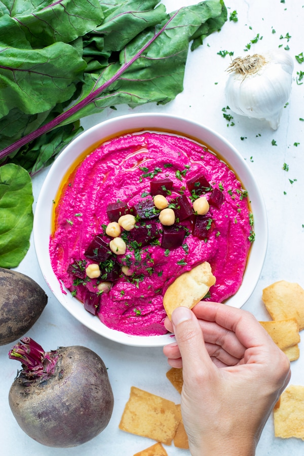 A hand dipping a chip into beet hummus for a healthy and easy to make appetizer or snack.