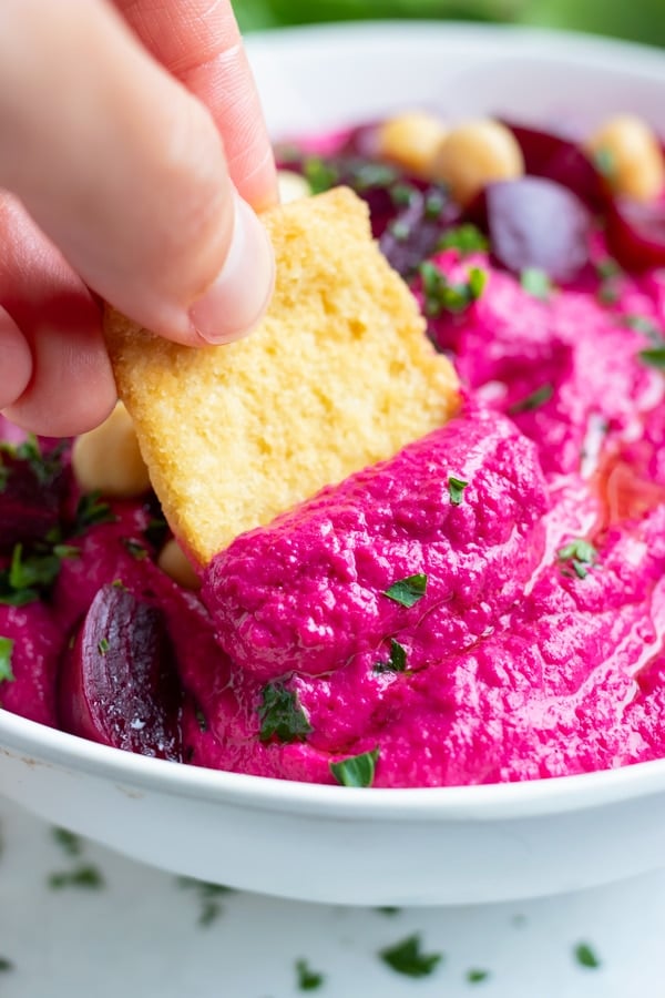 A gluten-free cracker is dipped into this creamy, homemade hummus.