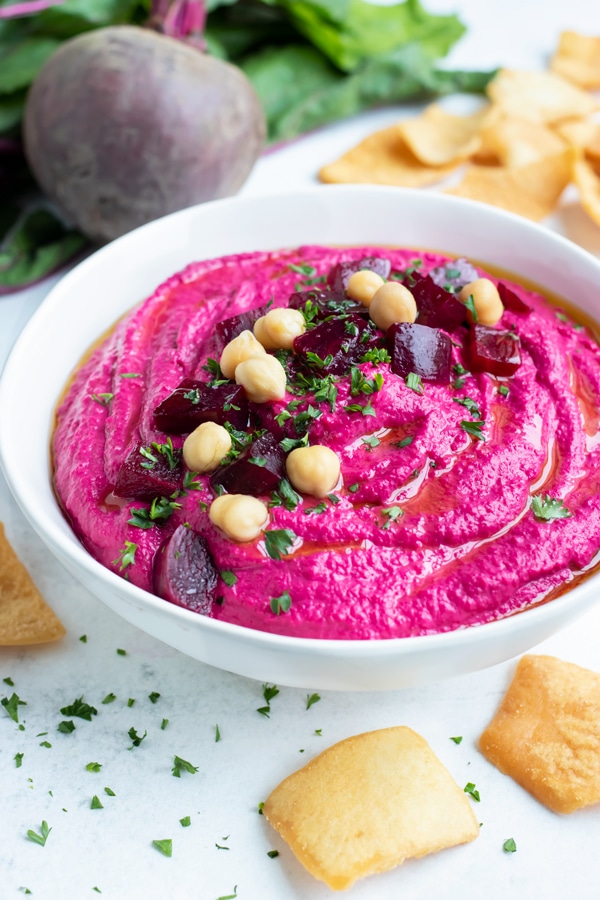 Vegan beet hummus recipe is served in a bowl with crackers or vegetables for a healthy snack.