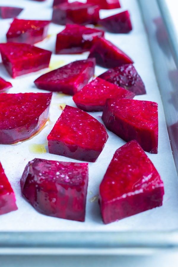 Cubed beets are roasted in the oven with olive oil on a baking sheet.