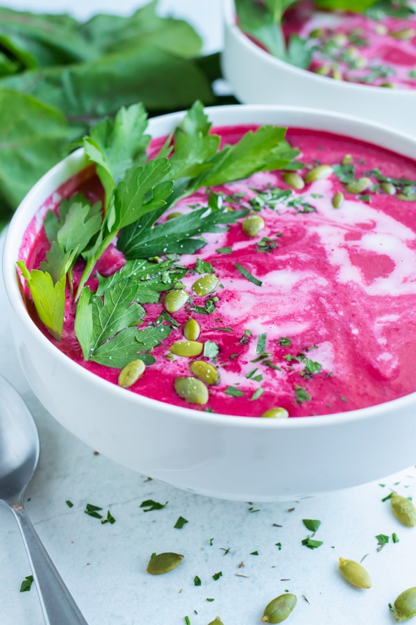 A white bowl full of a vegan and creamy beet soup recipe with cilantro and pumpkin seeds on top.