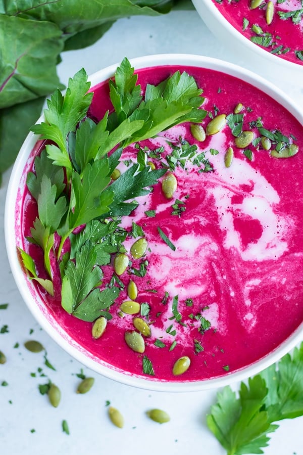 Creamy Beet Soup RECIPE in a white bowl at an overhead angle with garnishes like greens and seeds.