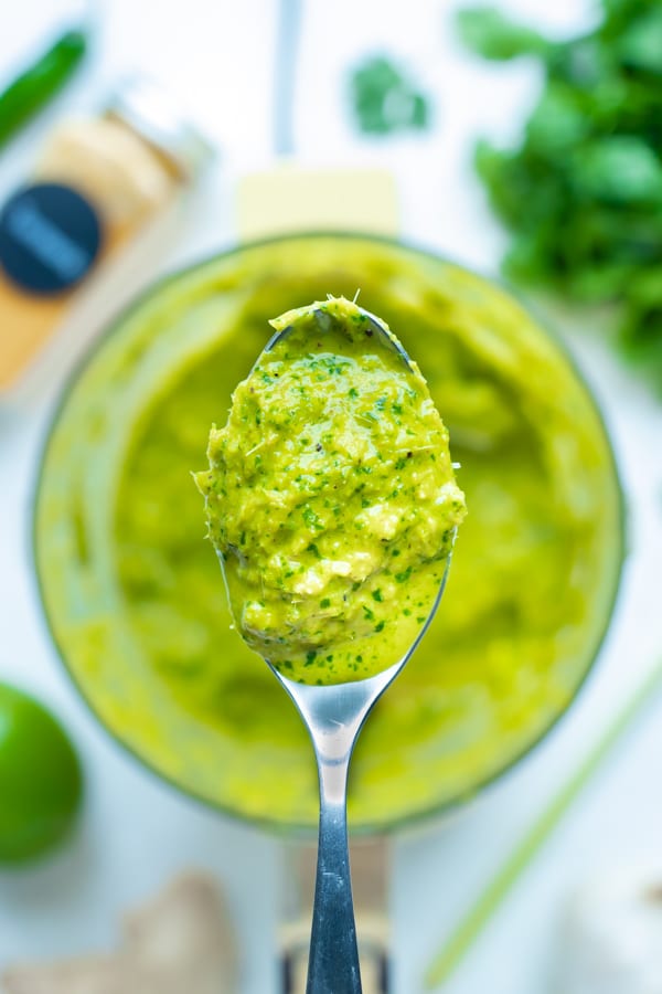 The best homemade Thai green curry paste is lifted up with a spoon.