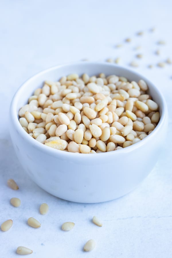 A small bowl full of golden brown roasted pine nuts to be used in a homemade pesto or salad.