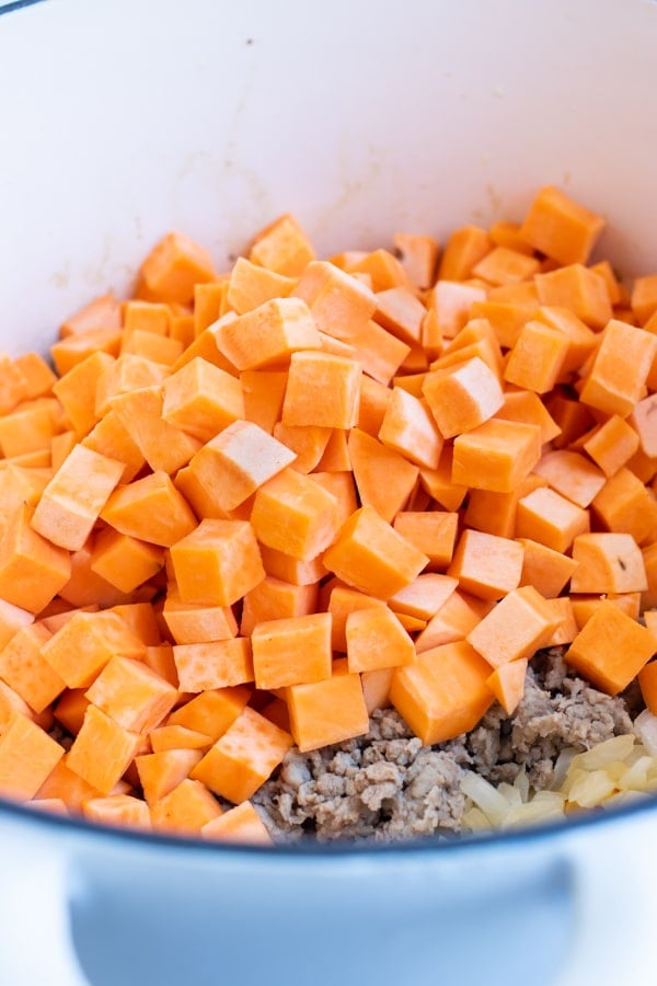 Cubed sweet potatoes are added tp the onion and ground turkey mixture in the dutch oven on the stove.