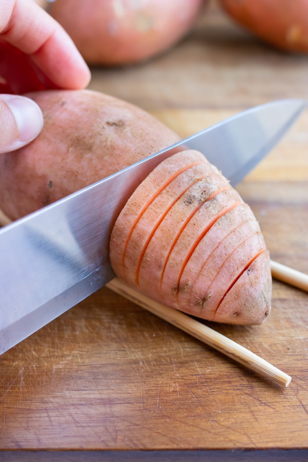 Sweet potato is sliced using a knife and chopsticks.
