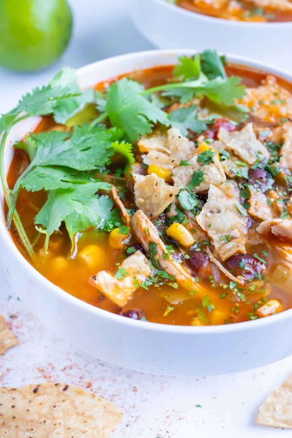 Quick and easy chicken tortilla soup is topped with fresh cilantro, lime juice, and tortilla chips.