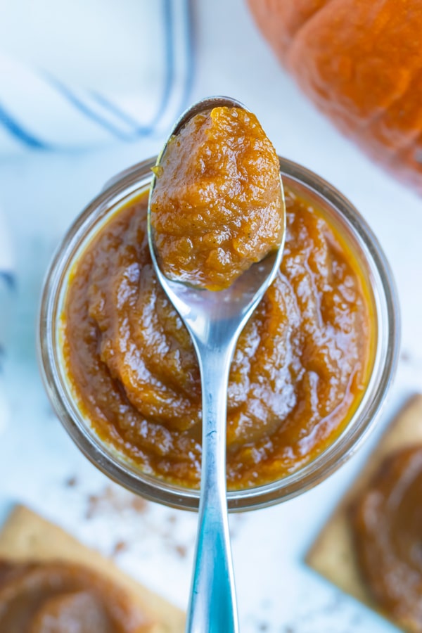 Vegan pumpkin butter is lifted by a spoon before spreading on a piece of bread.